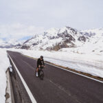Radfahrer radeln den steilen, verschneiten Passo Gavia hinauf, der im Juni von hoch aufragenden Schneewänden flankiert wird – ein seltener und atemberaubender Anblick.