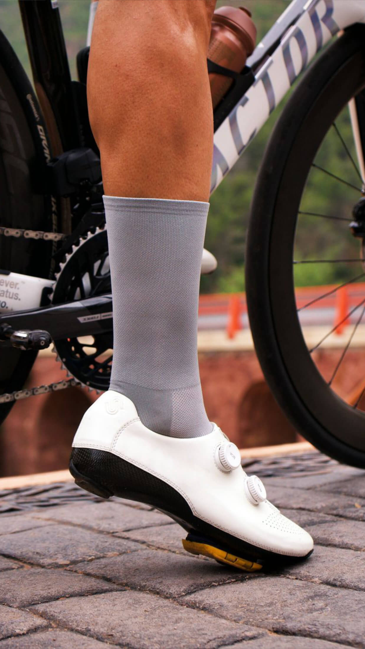 Close-up of cyclist’s foot in white cycling shoe wearing nologo classic gray cycling socks, next to the crankset of a white performance road bike.