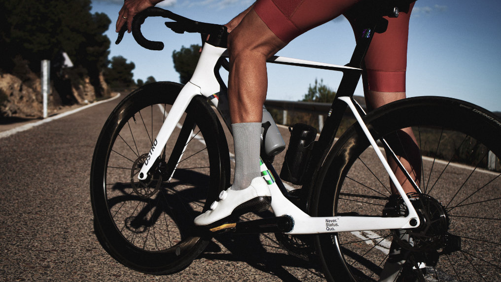 Cyclist wearing classic nologo gray cycling socks and red kit on a white road bike, captured mid-ride on a sunlit mountain road.