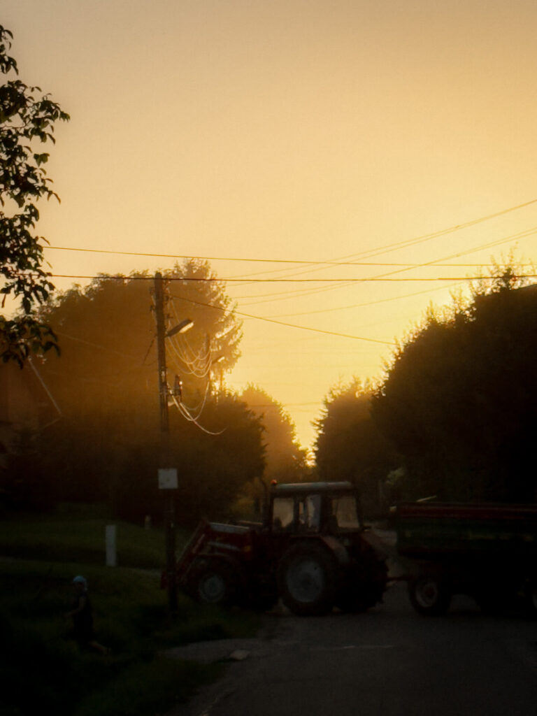 Tractor crossing a village road at sunset in Subcarpathia, warm golden light in the background