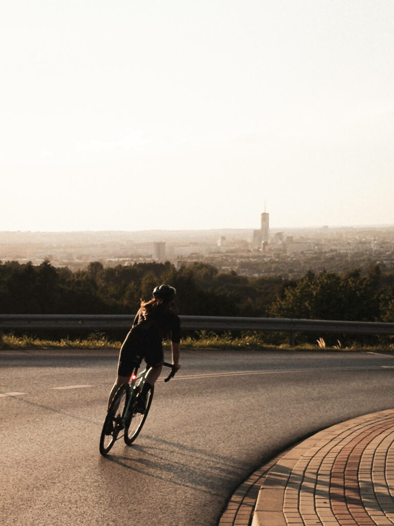 Cyclist descending a road curve with a city skyline in the distance during sunset
